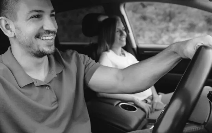 Man smiling driving a car with a woman smiling in the passenger seat